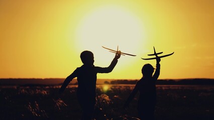 Children boy play with toy airplane outdoors, Silhouette. Child pilot runs with toy plane across...