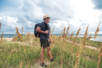 An adult man photographer in a straw hat and shorts stands on the sand dunes of the ocean. behind...