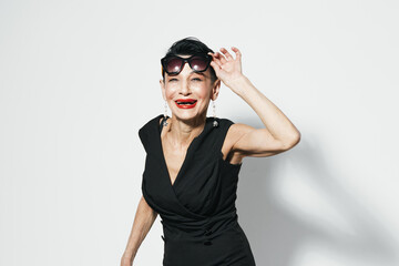 Elegant woman with red lipstick posing in black dress in front of white wall for camera portrait photo shoot