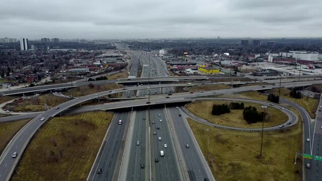Aerial shot of a drone flying over slightly busy Toronto 401 Highway on a cloudy day. Camera shows a road interchange with relatively moderate traffic speeding. Drone moving backward.