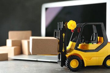 Toy forklift with box near laptop on table. Logistics and wholesale concept