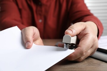 Man with papers using stapler at wooden table, closeup