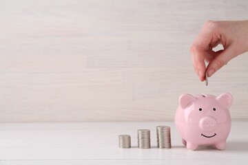 Financial savings. Woman putting coin into piggy bank at white wooden table, closeup. Space for text