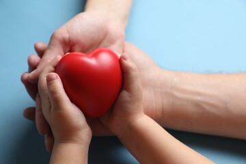 Father and his child holding red decorative heart on light blue background, closeup