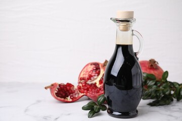 Tasty pomegranate sauce in bottle, fruits and branches on white marble table, closeup. Space for text