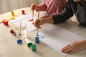 Little children drawing with brushes at wooden table indoors, closeup