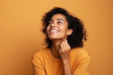 happy african american woman touching chin and looking up on orange background