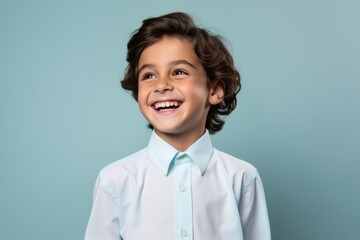 Cheerful little boy in white shirt looking at camera and smiling against blue background - Powered by Adobe