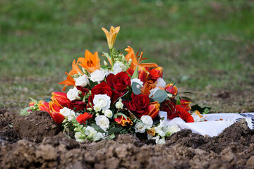 a flower arrangement with white and red roses, fire lilies and a mourning ribbon lies on the earth...