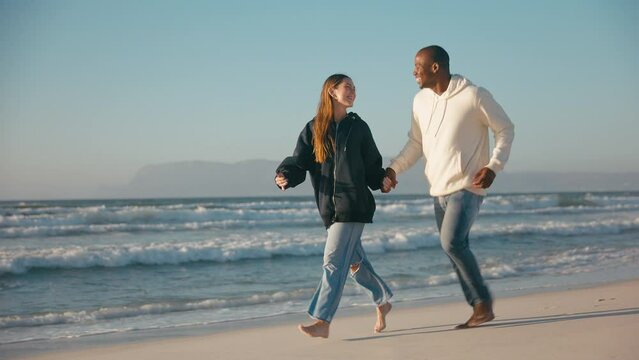 Camera tracks full length shot of casually dressed loving young couple running hand in hand along sandy shoreline of beach and sea in South Africa - shot in slow motion