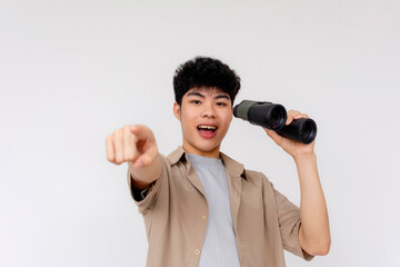 Naklejka premium Enthusiastic young Asian man with a surprised expression pointing forward and looking through binoculars on a clear background.