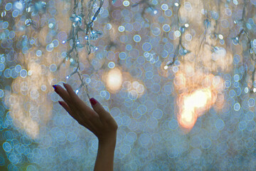 A woman hand is touching hanging line of LED light with sunset bokeh in an evening