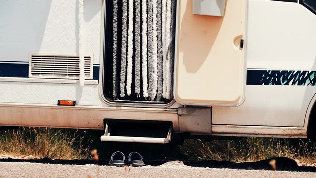 Camper detail. Shoes in front of caravan step and door curtain as insect screen. Camping on nature. Holidays and travel in motor home.