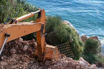 Excavator at work on a coastal construction site, with the Mediterranean Sea in the background and a clear sky