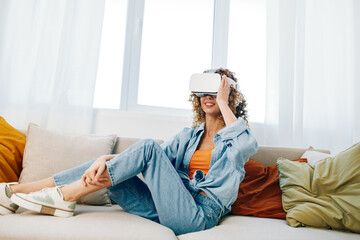 Smiling Woman Enjoying Virtual Reality Game at Home with VR Glasses on Sofa in Futuristic Living...