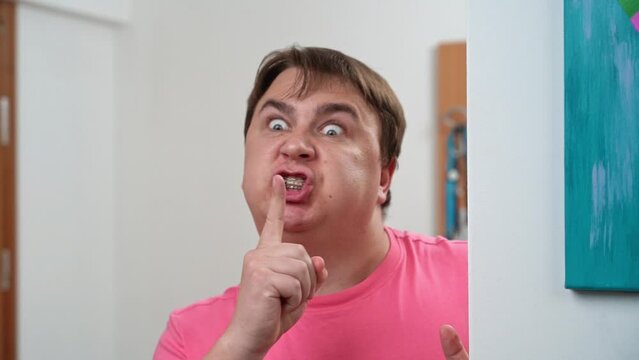 Angry, strict parent peeking out from behind wall puts hands to lips with gesture demanding silence, rolling his eyes to express dissatisfaction Incontinent man, father grabs children for making noise