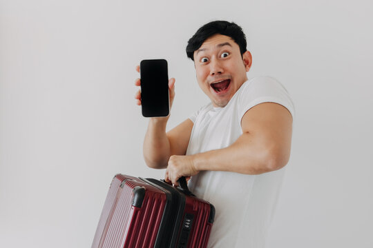 Wow face Asian man holds up a suitcase and a cell phone. He seems to be ready to travel with his mobile application.