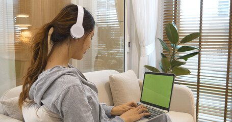 Happy asian woman use headphones listen to music online web conference sitting on cozy sofa in...