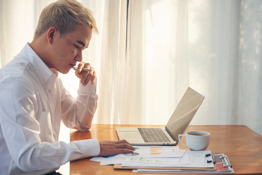 Portrait Asian Businessman typing laptop computer drinking coffee cup at office desk via wireless internet technology working online. Asian handsome man Freelance business person confident manager