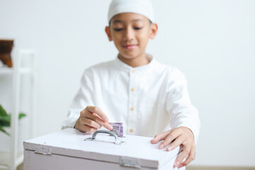 Young moslem boy putting money into donation box at mosque