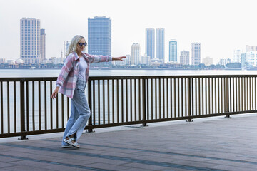 happy beautiful fashion mature woman enjoying view of modern city and dancing  at the seaside promenade.