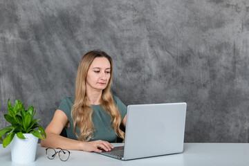 Young woman in glasses and gray dress making funny faces next to a laptop and green flower
