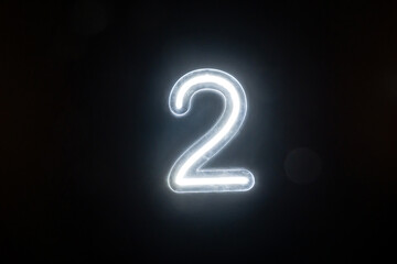 Number two glowing on the dark background. Close up of bright number 2
