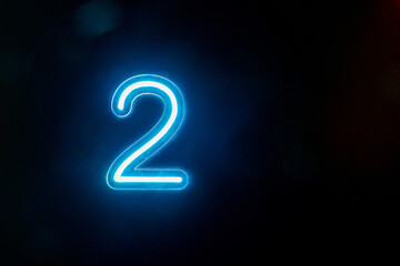 Number two glowing on the dark background. Close up of bright number 2