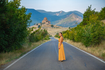 Woman Walking in Orange Dress Amidst Rural Landscape with Distant Mountain and Church