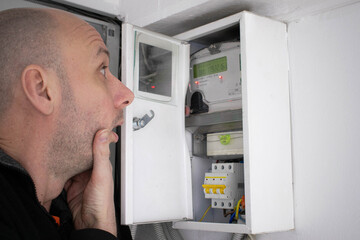 Bald man surprised by the electric meter readings. The concept of the energy crisis and large payments for electricity. - obrazy, fototapety, plakaty