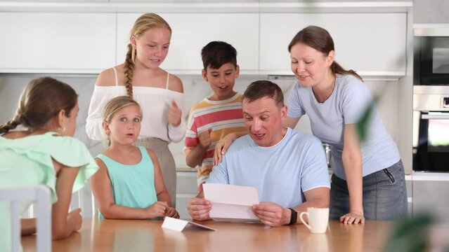 Happy satisfied large family reading documents together while sitting at the table at home 