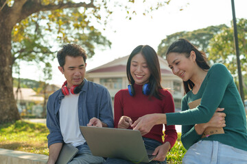 Group of Asian university students with headphones studying outdoor learning Make data reports from laptop learning and education concept Concepts of teenagers and people in the online world.