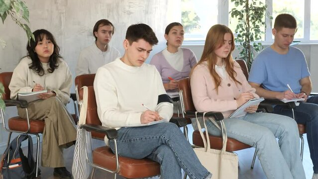 High school students listening to lesson with interest and taking notes sitting on chairs in lecture room