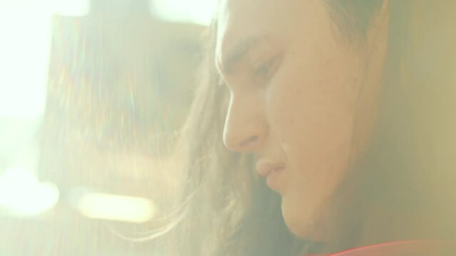 Young emotional musician with long curly hair playing the guitar and feeling music in sunlit room. Close-up view
