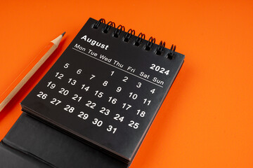 August 2024 desk calendar with pencil on orange background.