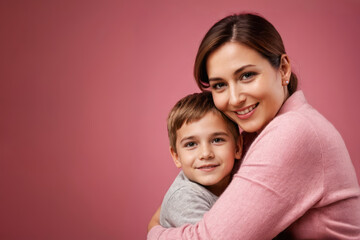happy woman hug her son on pink background with copy space. Concept of Mothers day