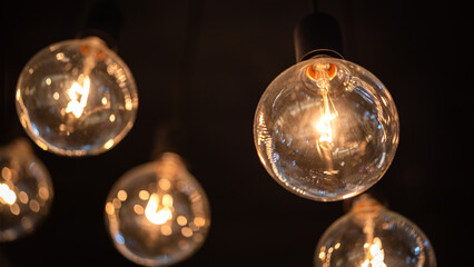 Classic sphere lighting bulbs are glowing in orange warming shade, there are hanging from ceiling...
