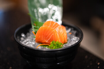 Piece of freshness raw salmon sashimi which are placed on ice, serve in the black bowl. Food object photo, close-up and selective focus.