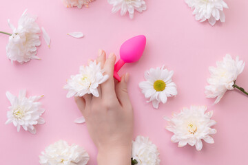 Woman hand touch sex toy plug on pink background with flowers. flat lay