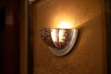 A classic luxury designed wall lamp with corridor as blurred background. Interior decoration object with selective focus. Photo contained noise due to high contrast ratio between light and shadow.