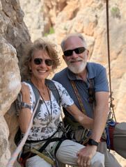 Mature active couple posing in the middle of climbing a rock face