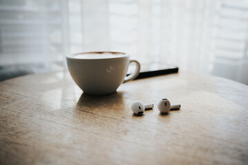 Pair of white wireless headphones for smartphone and coffee cups on wooden table. Vintage tone. Relaxation concept.