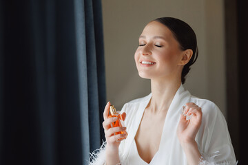 Happy young woman with makeup use perfume, radiant bride smiling. Concept morning and getting ready...
