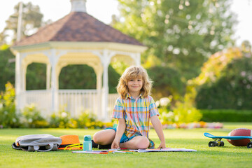 Little artist drawing painting art in park. Cute child boy with books and pencil writing on notebook outdoors. Kids outdoor learning and education concept. Summer vacation homework.