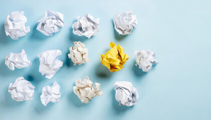 A standout yellow crumpled paper among numerous white ones on a light blue background, symbolizing ideas, brainstorming, and creativity.
