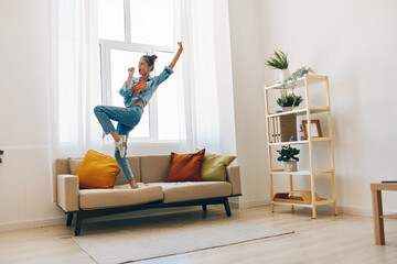 Joyful Woman Jumping with Music, Smiling and Having Fun on Sofa in Relaxing Home