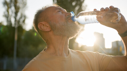 Close up older man drinking clear mineral water morning sun rays thirsty male drink pure aqua...