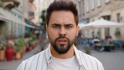 Close up angry Caucasian man frowning eyebrows city street outside dissatisfied displeased...
