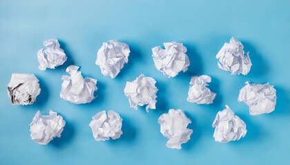 Crumpled white paper balls scattered randomly on a light blue background, symbolizing ideas, brainstorming, and creativity.