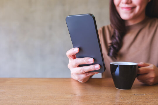 Closeup image of a young woman holding and using mobile phone while drinking coffee